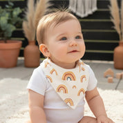 Bandana babador para bebê com estampa de arco-íris boho em algodão premium, fundo off-white, modelo unissex.