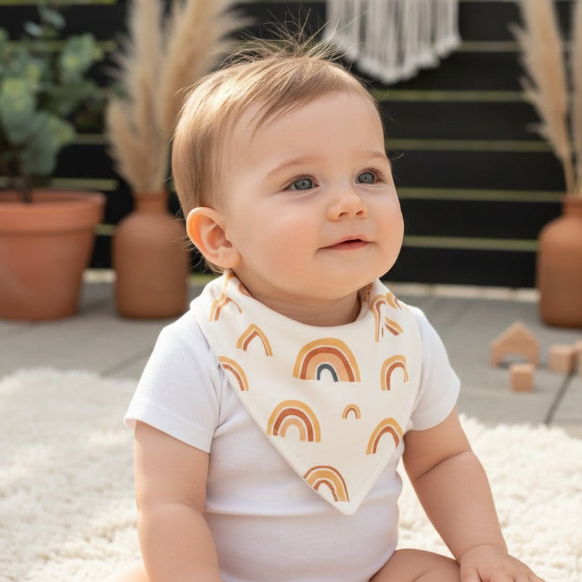 Bandana babador para bebê com estampa de arco-íris boho em algodão premium, fundo off-white, modelo unissex.
