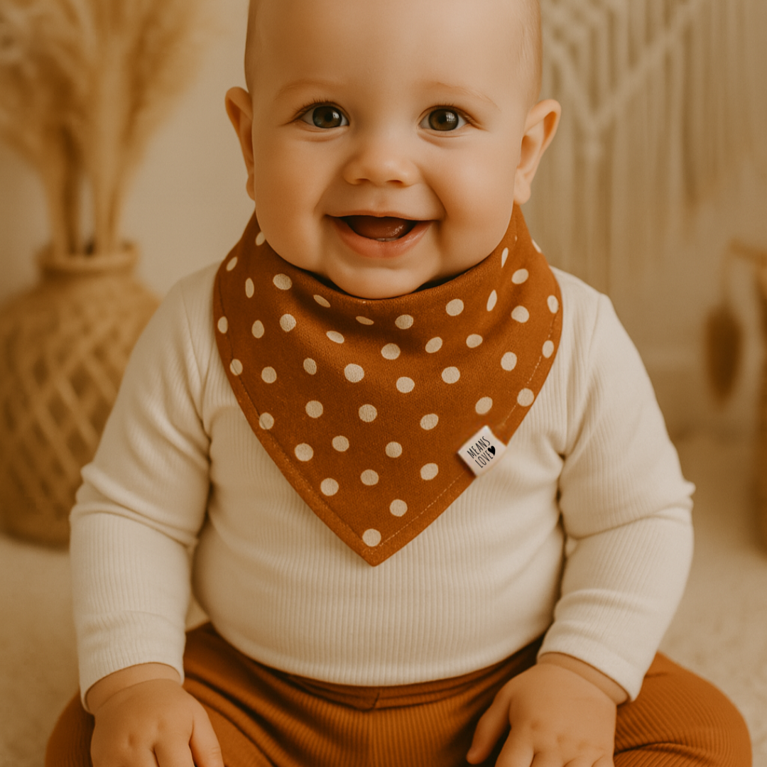 Bebê de 12 meses usando bandana babador unissex estampada em poá caramelo, em ambiente natural com elementos boho, transmitindo conforto e sofisticação.