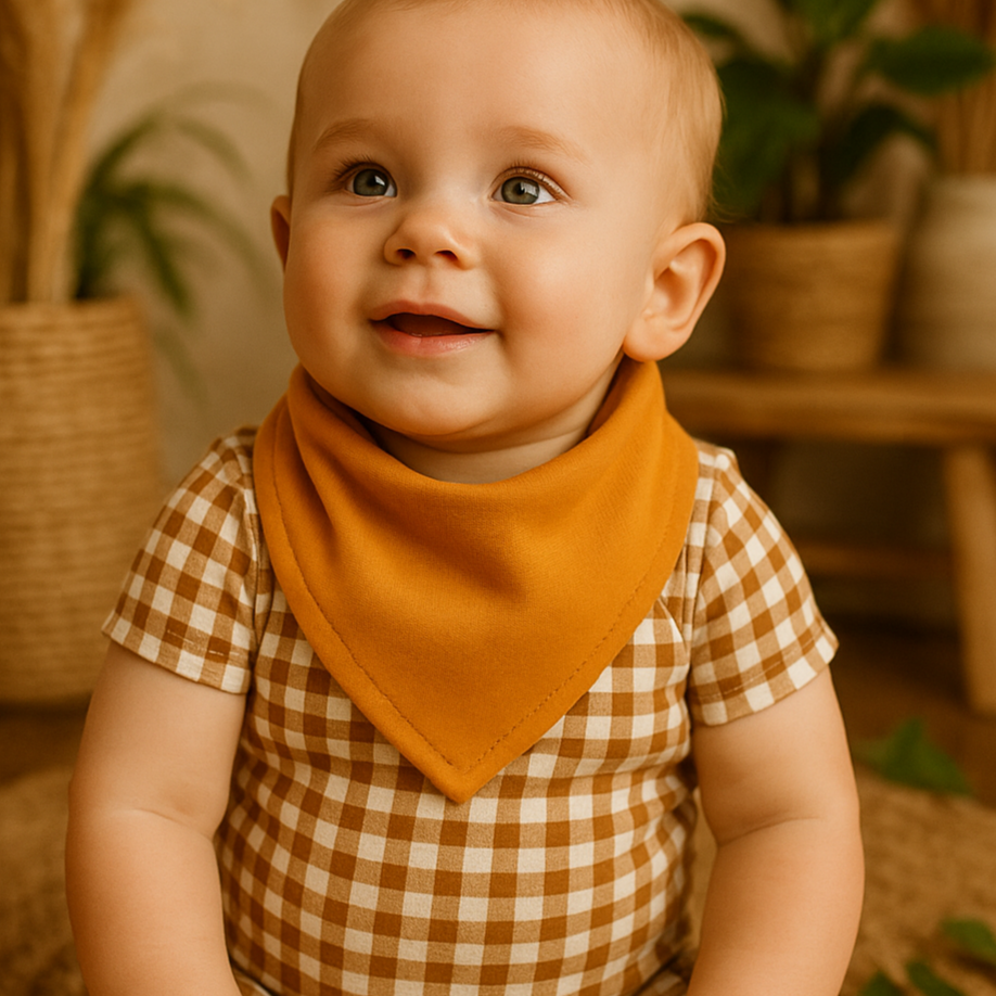 Bebê de 9 meses usando bandana mostarda em ambiente boho chic com luz natural, madeira e plantas ao fundo

