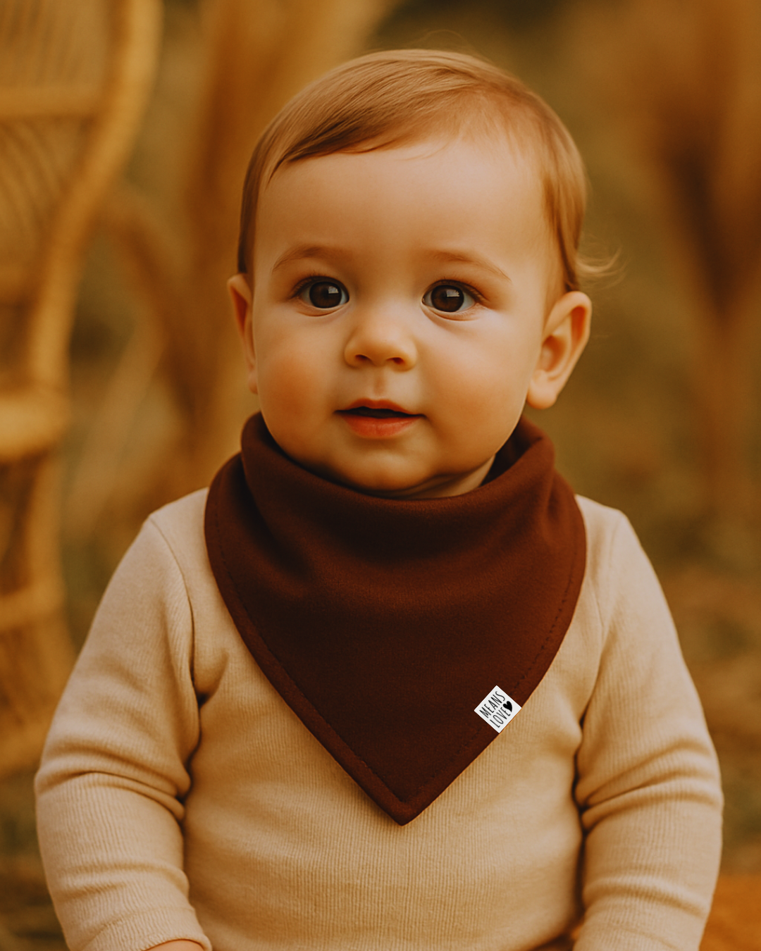 Bebê de 9 meses com bandana babador marrom café da Means Love Baby, vestindo body bege claro em cenário natural com luz suave e elementos boho.

