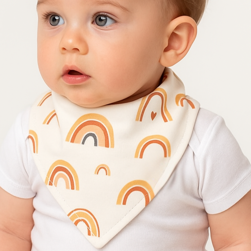 Bandana babador para bebê com estampa de arco-íris boho em algodão premium, fundo off-white, modelo unissex.