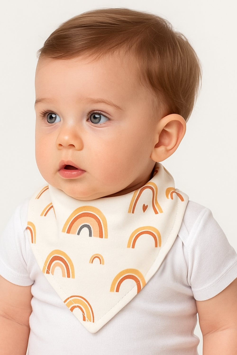 Bandana babador para bebê com estampa de arco-íris boho em algodão premium, fundo off-white, modelo unissex.