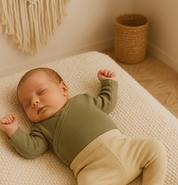 Bebê recém-nascido usando body kimono verde oliva de algodão stretch, deitado em ambiente aconchegante com luz suave.