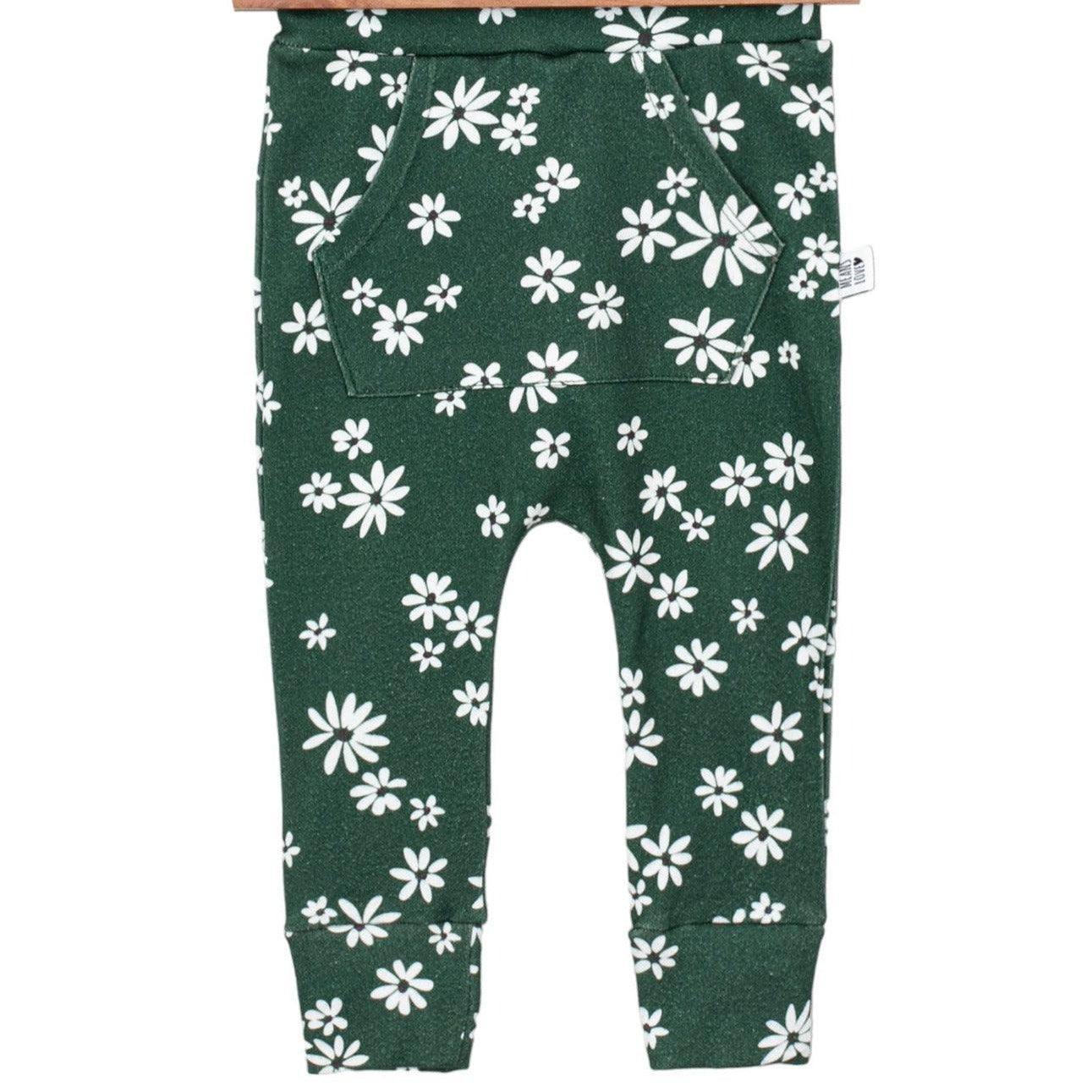 Bebê pequeno de pé sobre tapete de linho bege, usando calça verde com estampa floral branca da coleção Daisy da Means Love Baby.

