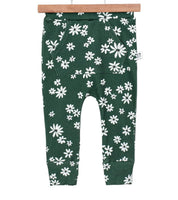 Bebê pequeno de pé sobre tapete de linho bege, usando calça verde com estampa floral branca da coleção Daisy da Means Love Baby.

