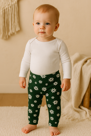 Bebê pequeno de pé sobre tapete de linho bege, usando calça verde com estampa floral branca da coleção Daisy da Means Love Baby.

