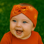 Faixinha de cabelo para bebê menina em algodão stretch com estampa boho exclusiva de sol e arco-íris em tons terrosos, modelo com frente cruzada da marca Means Love Baby.