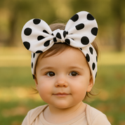 Bebê de 1 ano ao ar livre usando laço de cabelo infantil branco com estampa de poá preto e body neutro

