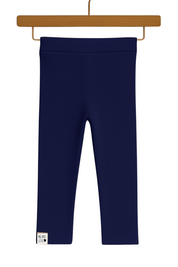 Legging infantil canelada azul marinho em algodão premium, com cós anatômico e modelagem confortável, pendurada em cabide de madeira sobre fundo neutro boho.

