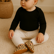 Legging off white para bebê em algodão premium canelado, pendurada em cabide de madeira, estilo minimalista.