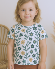 Menina de 3 anos usando camiseta infantil floral antigo da Means Love Baby em ambiente elegante.

