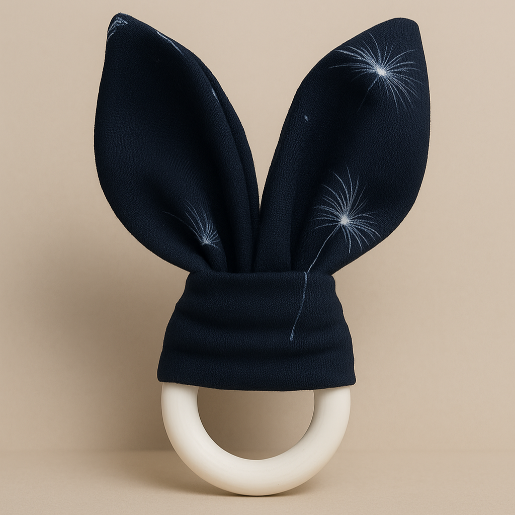 Mordedor de madeira para bebê com orelhinhas de algodão azul marinho estampadas com dente-de-leão, fundo neutro elegante estilo catálogo