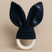 Mordedor de madeira para bebê com orelhinhas de algodão azul marinho estampadas com dente-de-leão, fundo neutro elegante estilo catálogo