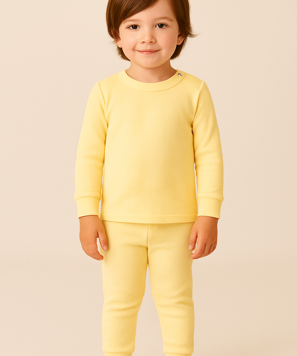 crianca de 4 anos usando pijama amarelo canelado de duas peças em ambiente boho chic com luz natural e elementos como madeira e plantas.

