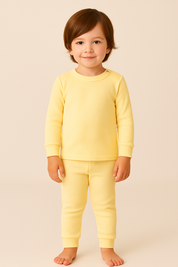 crianca de 4 anos usando pijama amarelo canelado de duas peças em ambiente boho chic com luz natural e elementos como madeira e plantas.

