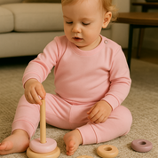 Bebê de 4 meses usando pijama rosa canelado de duas peças em ambiente boho chic com luz natural e elementos como madeira e plantas.