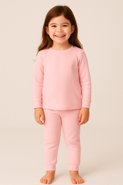 crianca de 4 anos usando pijama rosa canelado de duas peças em ambiente boho chic com luz natural e elementos como madeira e plantas.

