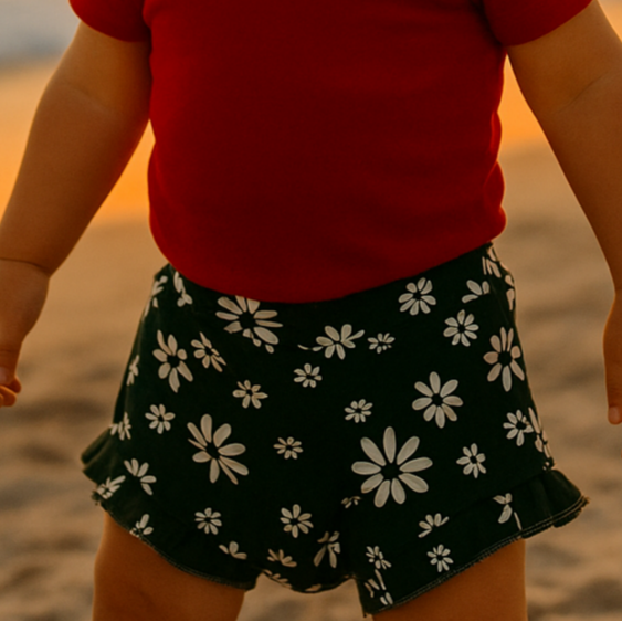 menina vestindo shortinho plissado bebe menina verde com margaridas na brancas na beira da praia num final de tarde